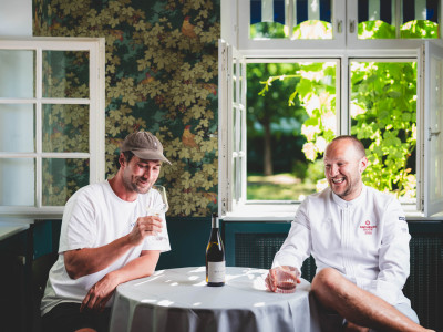 Christoph Düster und Christoph Schneider sitzen mit einer flasche Wein an einem runden Tisch.