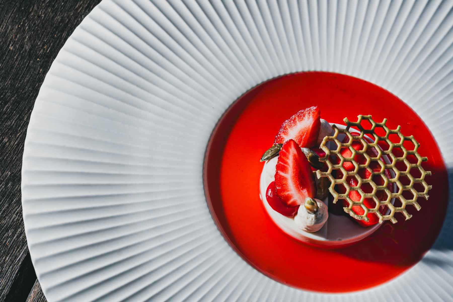 Ein rotes Dessert mit Erdbeeren und roter Sauce auf einem weißen, edlen Teller.