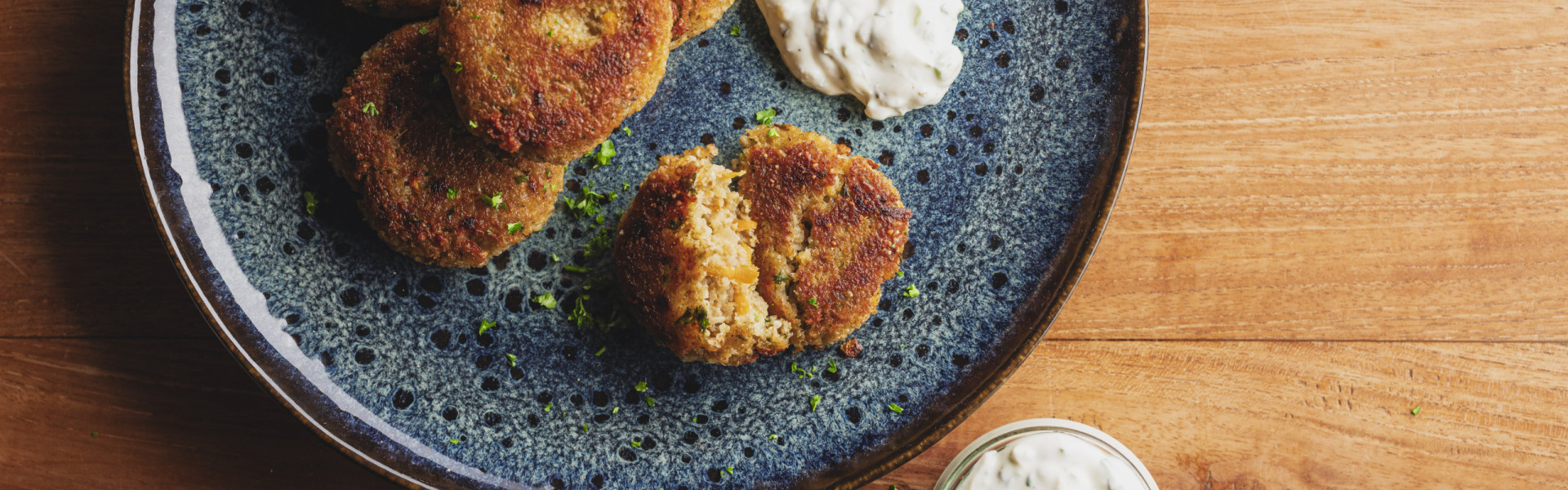 Blauer Teller mit Grünkernbratlingen und Kräuterquark auf einem Holztisch