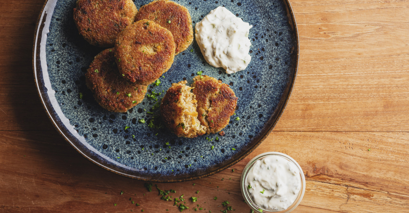 Blauer Teller mit Grünkernbratlingen und Kräuterquark auf einem Holztisch