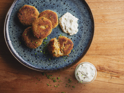 Blauer Teller mit Grünkernbratlingen und Kräuterquark auf einem Holztisch