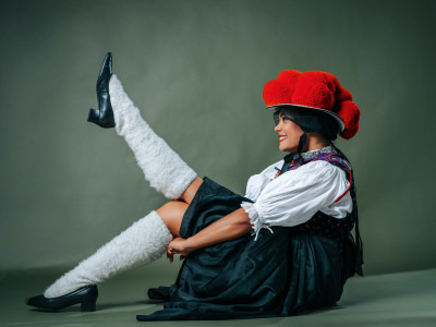Junge Frau in traditioneller Schwarzwälder Bollenhut-Tracht posiert mit Bein in die Luft und augenzwinkerndem Lächeln