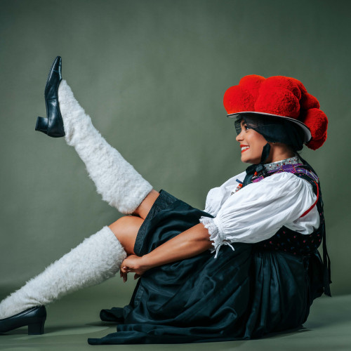 Junge Frau in traditioneller Schwarzwälder Bollenhut-Tracht posiert mit Bein in die Luft und augenzwinkerndem Lächeln