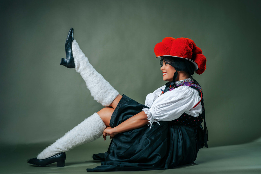 Junge Frau in traditioneller Schwarzwälder Bollenhut-Tracht posiert mit Bein in die Luft und augenzwinkerndem Lächeln