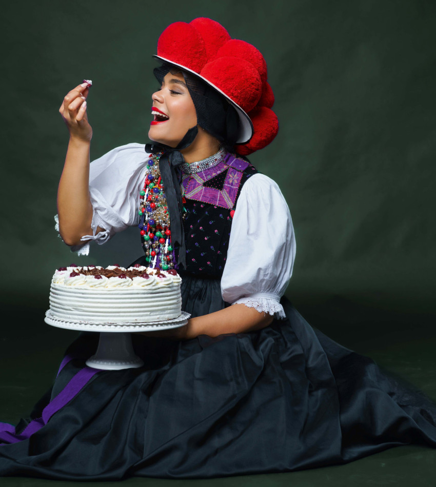 Junge Frau in Schwarzwälder Bollenhut-Tracht genießt ein Stück Schwarzwälder Kirschtorte mit einem Lächeln