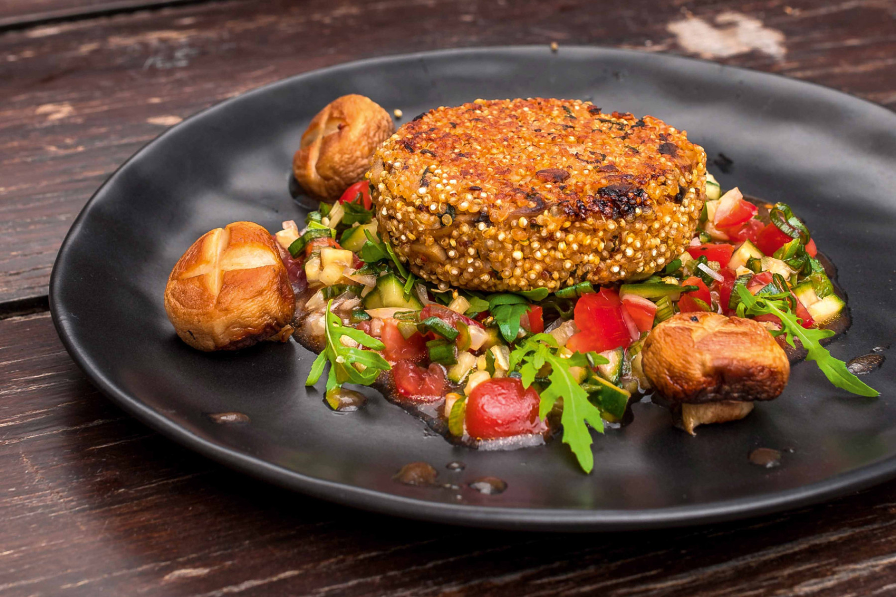 Quinoa-Champignon-Patty an Weizenbier-Gemüse-Salsa auf einem schwarzen Teller