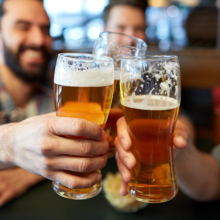 Drei Männer prosten sich mit Bier zu, zwei davon sind im Bild zu sehen