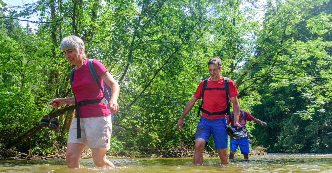 Drei Menschen in sommerlicher Kleidung waten durch Gewässer.