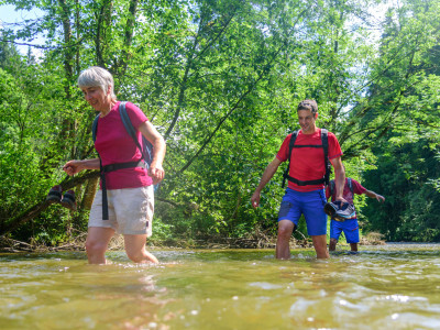 Drei Menschen in sommerlicher Kleidung waten durch Gewässer.
