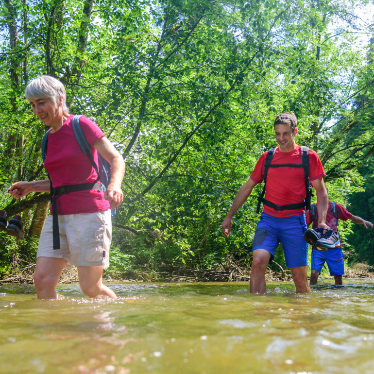 Drei Menschen in sommerlicher Kleidung waten durch Gewässer.