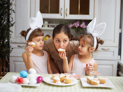 Eine Mutter mit Zwillingen beißt in einem Muffin, den ihr die Tochter hinhält