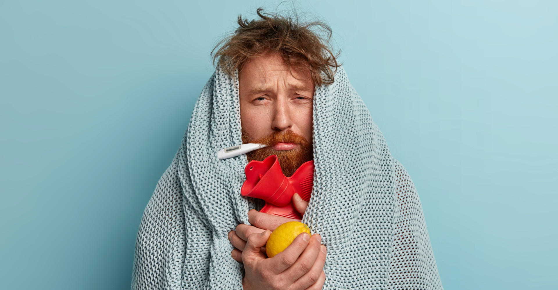 Mann mit Fieberthermometer im Mund und Orange (Vitamin C!) in der Hand. Schwer erkältet!
