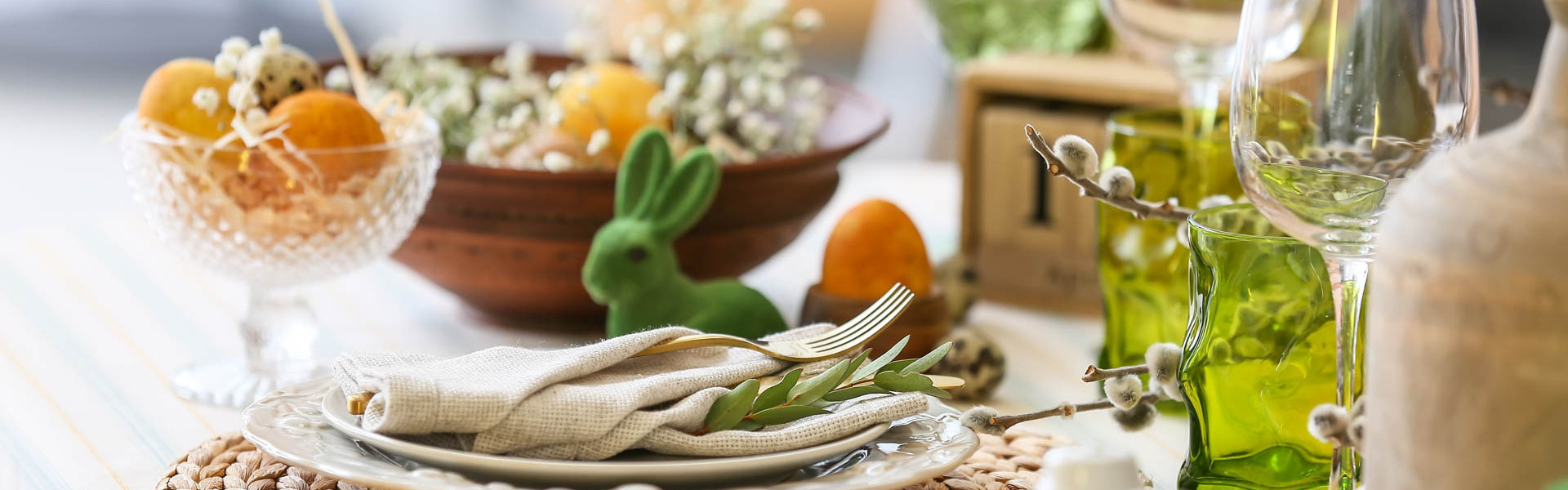 Gedeckter Tisch mit Tellern und Servietten und einem grünen Osterhasen und Frühlingsblumen