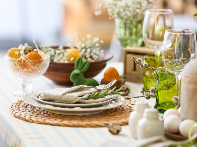 Gedeckter Tisch mit Tellern und Servietten und einem grünen Osterhasen und Frühlingsblumen