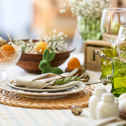 Gedeckter Tisch mit Tellern und Servietten und einem grünen Osterhasen und Frühlingsblumen