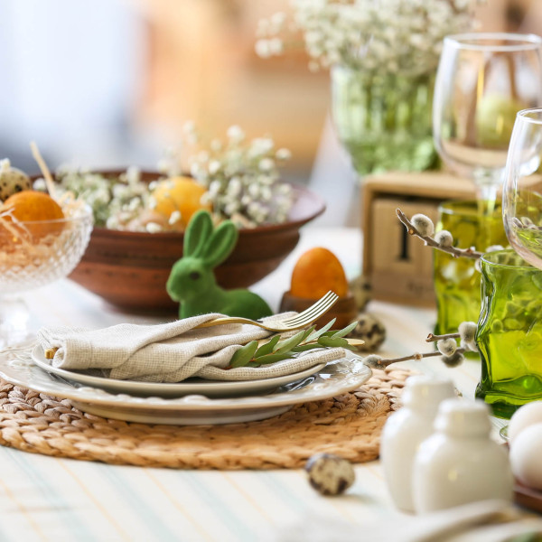 Gedeckter Tisch mit Tellern und Servietten und einem grünen Osterhasen und Frühlingsblumen