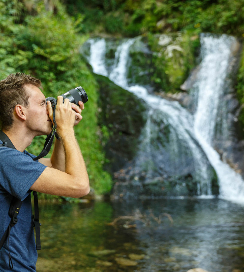 Ein junger Mann fotografiert einen Wasserfall.