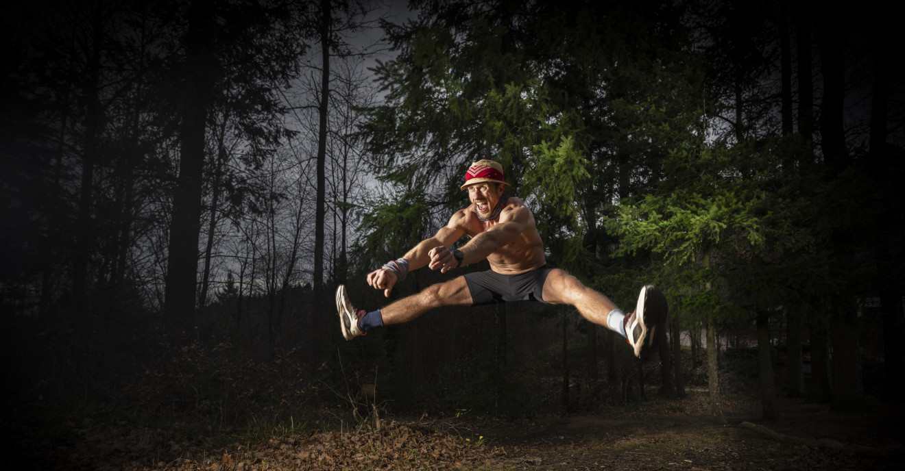 Ein Mann springt im Spagat über einen Ast