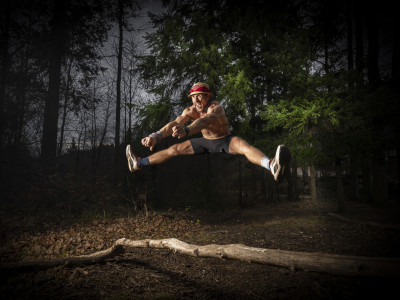 Ein Mann springt im Spagat über einen Ast