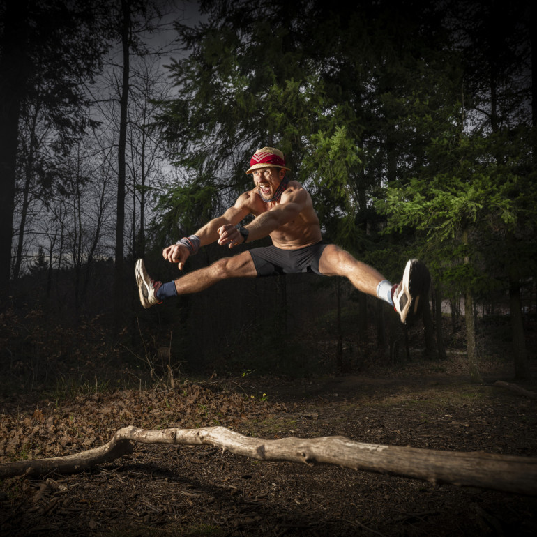 Ein Mann springt im Spagat über einen Ast