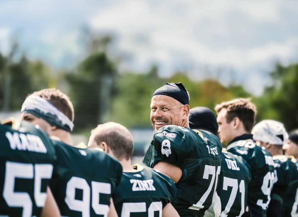 Footballspieler mit breitem Lächeln dreht sich in Spielerreihe um, Schulter an Schulter mit Teamkollegen beim Spieltag