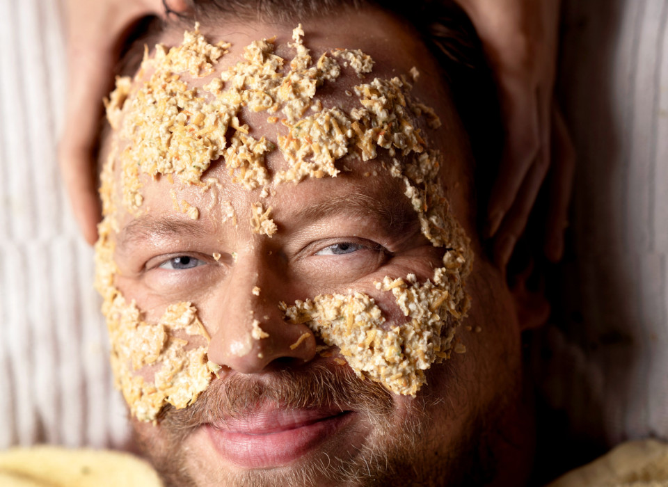 Mann mit Getreide-Gesichtsmaske lächelt entspannt während Wellnessbehandlung im Schwarzwald