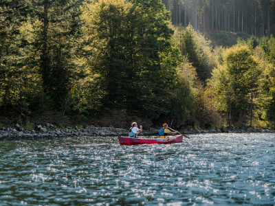 Zwei Menschen paddeln im roten Kanu entlang bewaldeter Ufer am Schluchsee im Schwarzwald