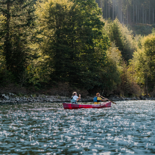 Zwei Menschen paddeln im roten Kanu entlang bewaldeter Ufer am Schluchsee im Schwarzwald