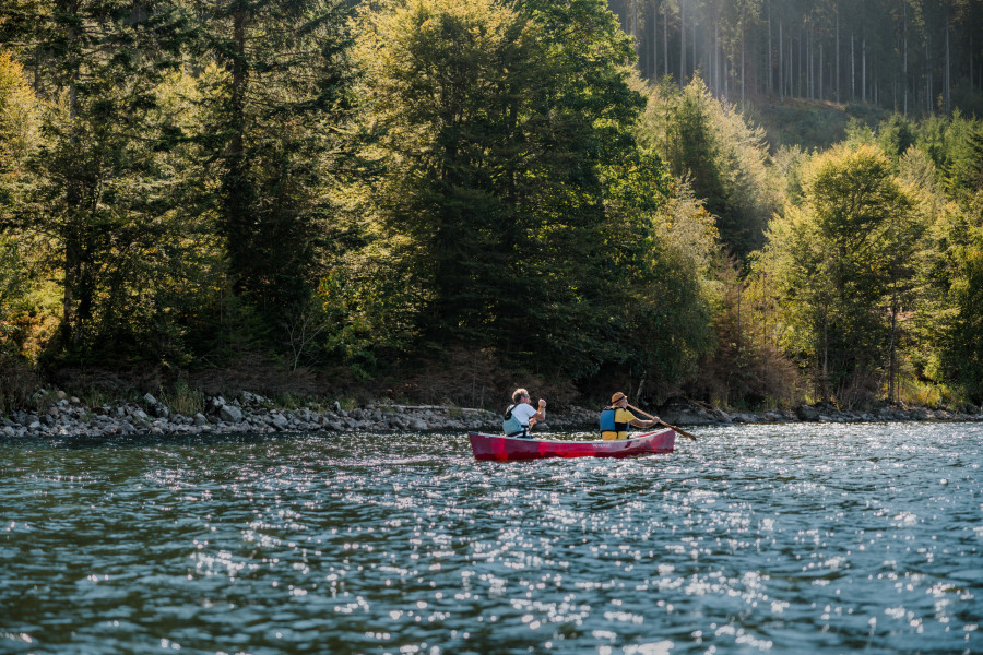 Zwei Menschen paddeln im roten Kanu entlang bewaldeter Ufer am Schluchsee im Schwarzwald