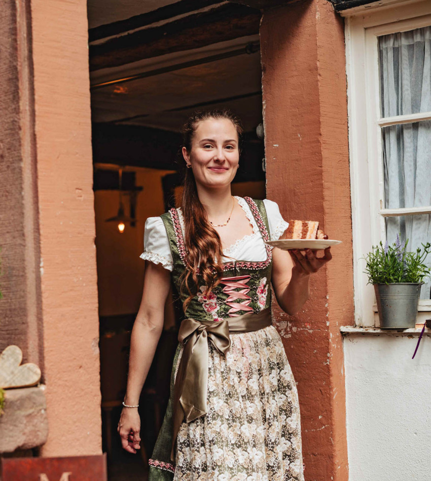 Eine junge Frau in Tracht trägt einen Teller mit einem Stück Torte.