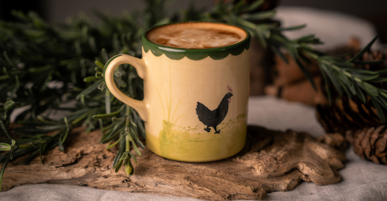 Eine Tasse mit "Hahn und Henne"-Dekor aus Keramik steht auf dem Tisch