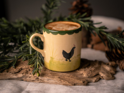 Eine Tasse mit "Hahn und Henne"-Dekor aus Keramik steht auf dem Tisch