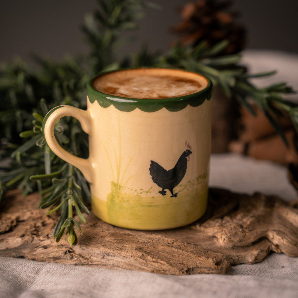 Eine Tasse mit "Hahn und Henne"-Dekor aus Keramik steht auf dem Tisch