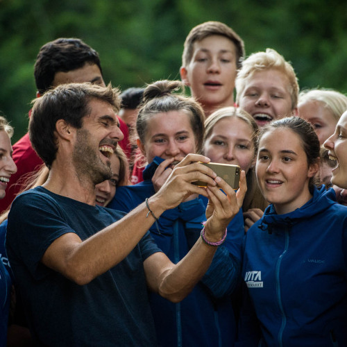 Eine Gruppe junger, vergnügter Menschen sieht sich gemeinsam etwas auf einem Smartphone an. Sie befinden sich in der Wildnis. 