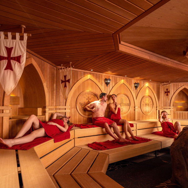 Eine Gruppe sitzt in einer mit Schwertern und Wappen geschmückten Sauna