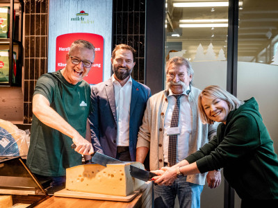 Vier Personen schneiden einen Laib Käse zur Eröffnung der Käsetheke an.
