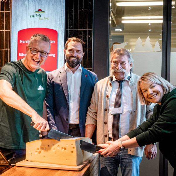 Vier Personen schneiden einen Laib Käse zur Eröffnung der Käsetheke an.