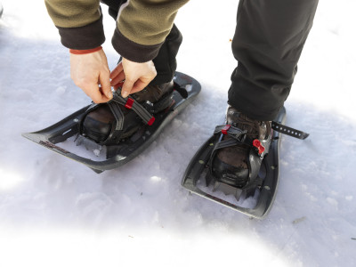 Eine Frau schnürt sich Schneeschuhe an die Füße