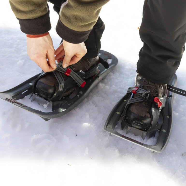 Eine Frau schnürt sich Schneeschuhe an die Füße