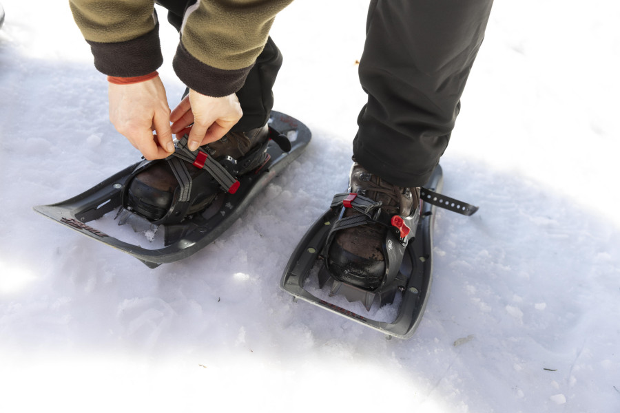 Eine Frau schnürt sich Schneeschuhe an die Füße