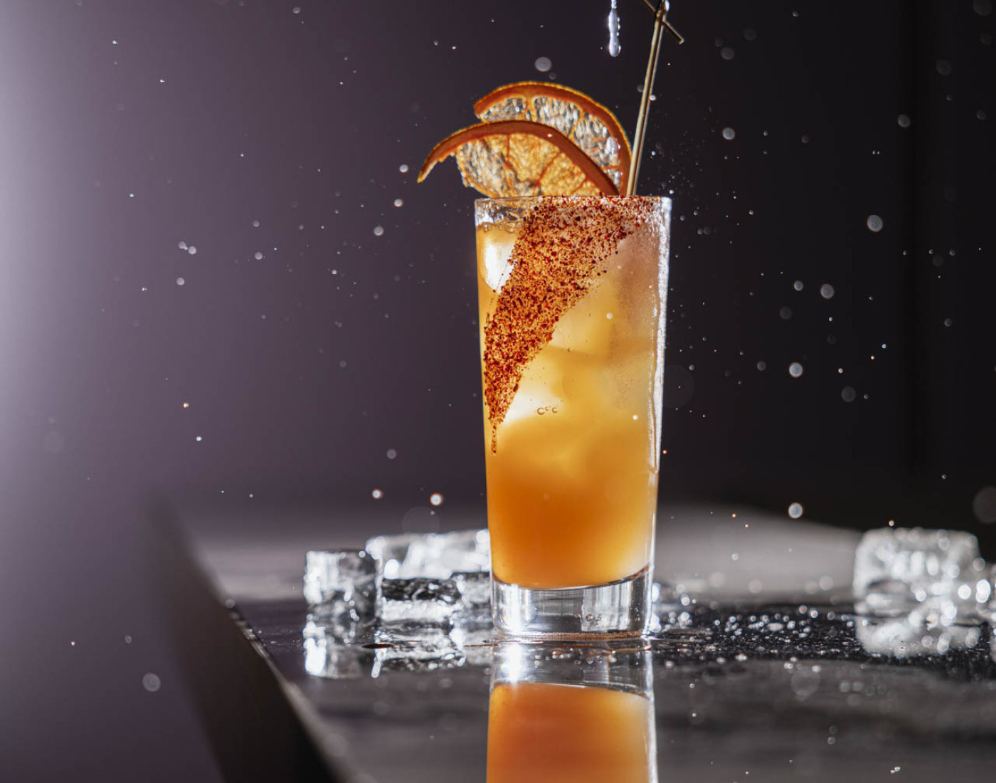 Ein orangener High-Ball-Cocktail mit Gewürzrand und getrockneten Orangenscheiben.