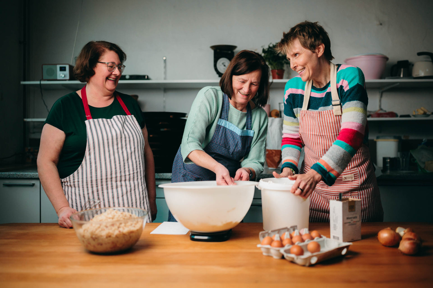 Drei Frauen mit Schürzen bereiten einen Zwiebelkuchen zu.