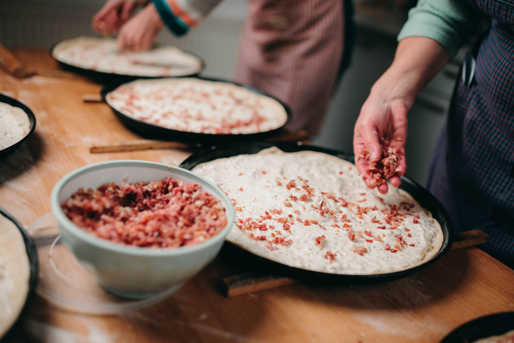 Drei Zwiebelkuchen werden mit Speck belegt.