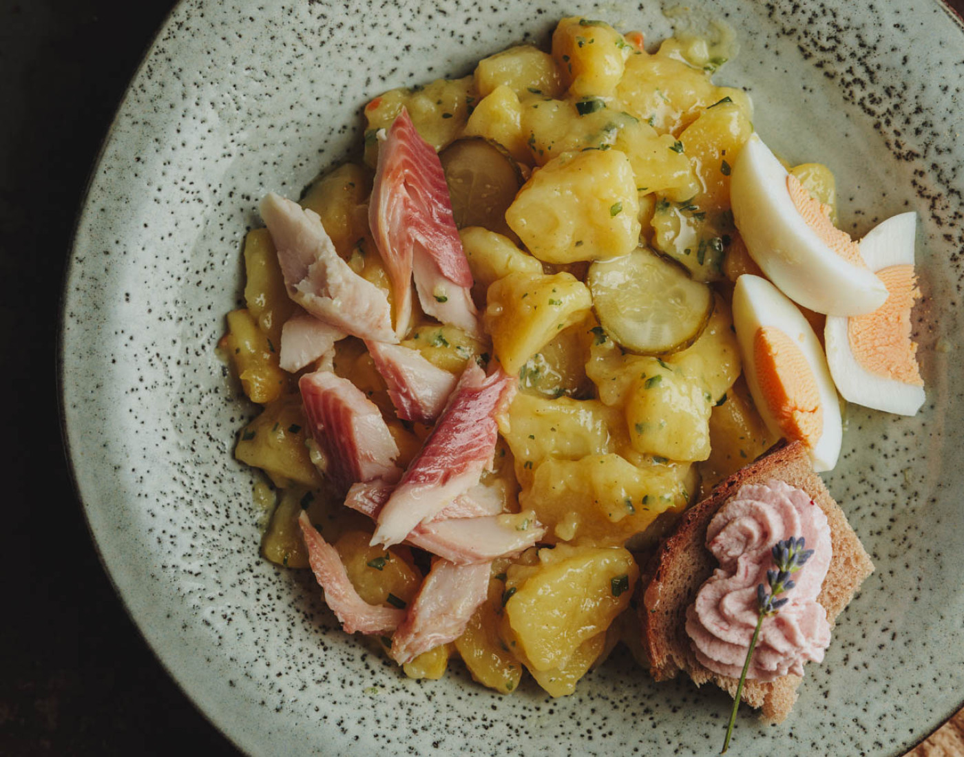 Kartoffelsalat mit gezupfter Forelle und drei halbierten, gekochten Eiern auf einem weißen Teller.