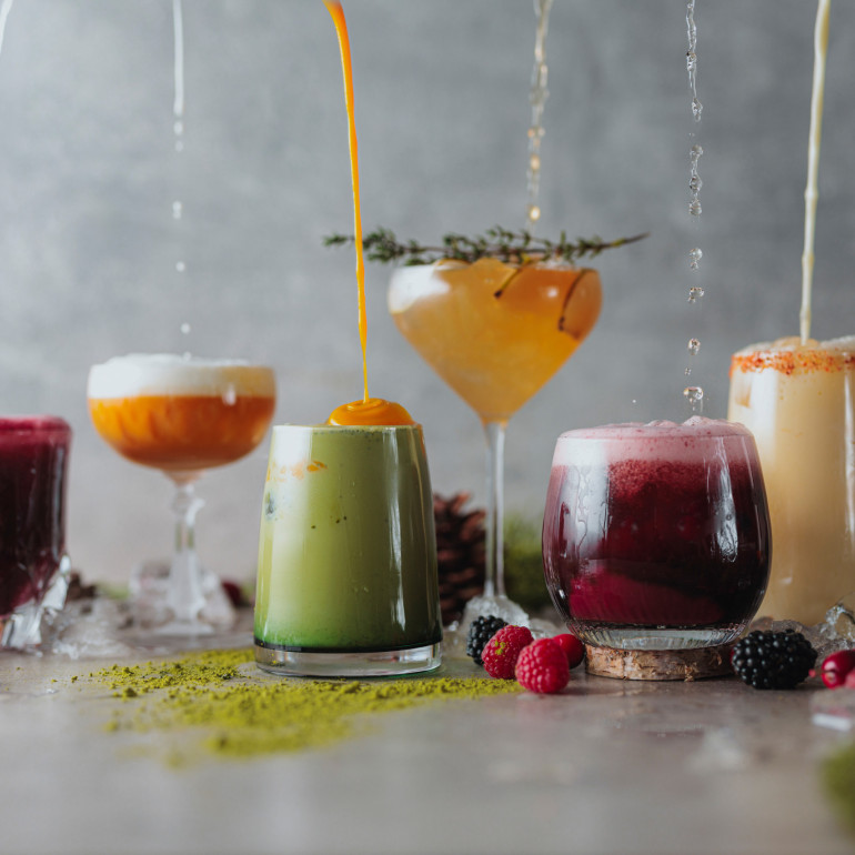 Sechs farbenfrohe Cocktails stehen in einer Reihe