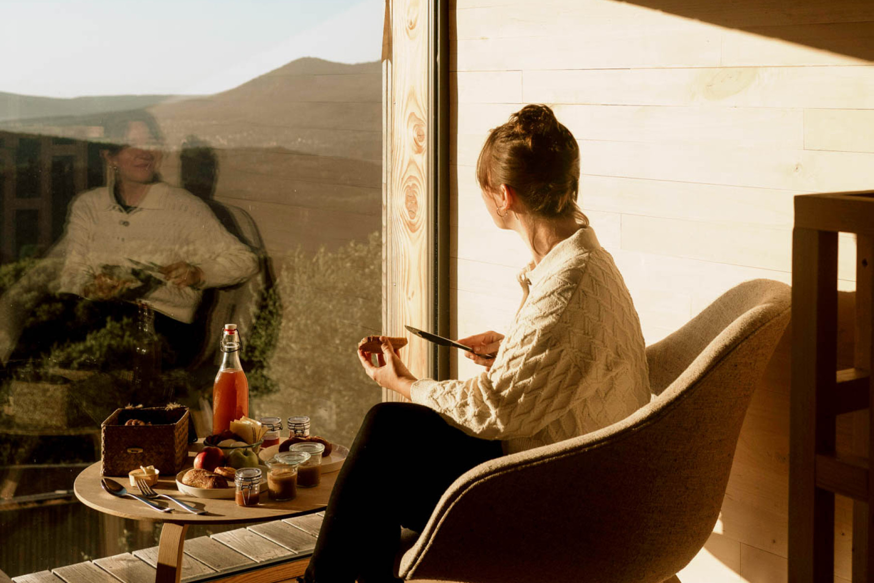 Eine Frau sitzt am Fenster einer Hytte des 48°Nord und frühstückt.