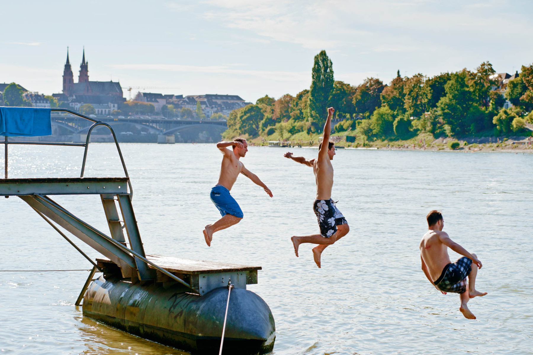 Drei junge Männer springen in den Rhein vom Basler Rheinufer.