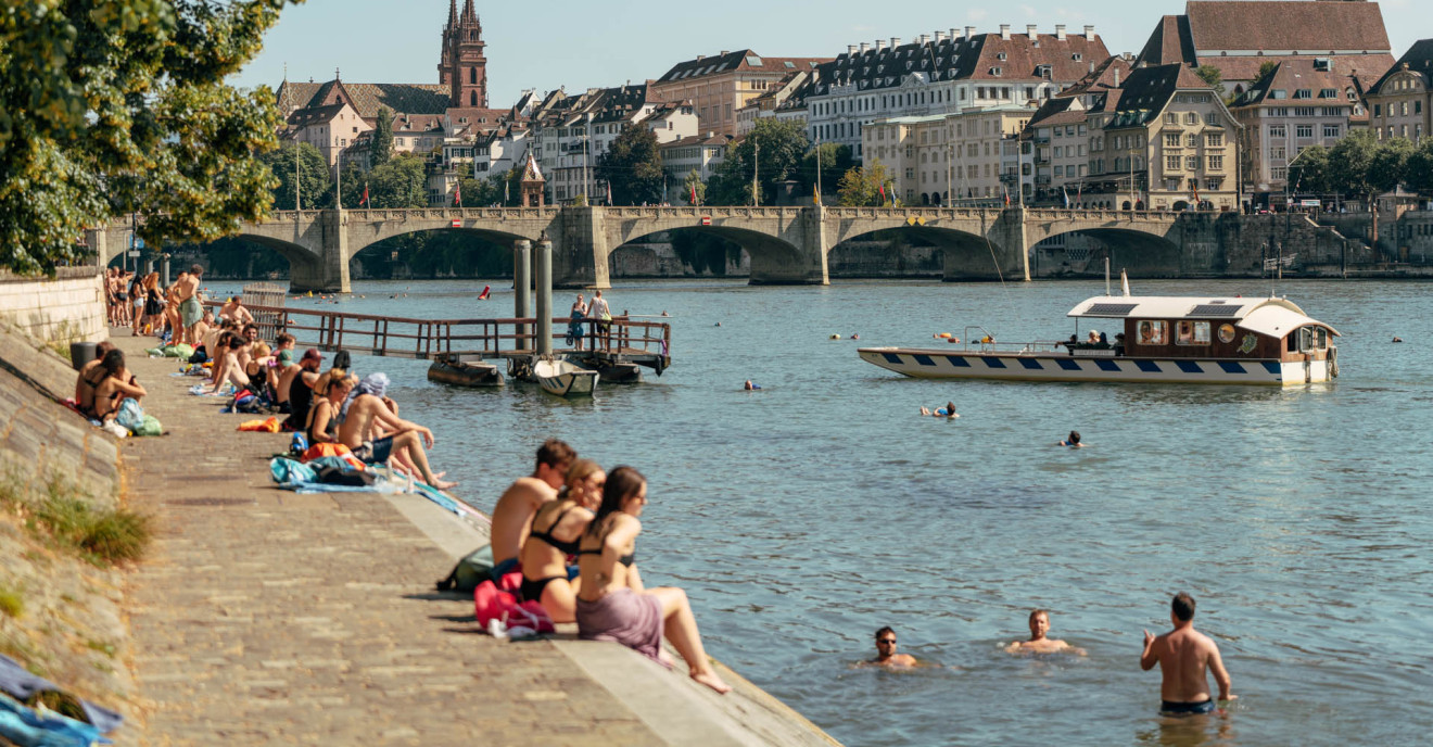 Badende Menschen im Rhein und am Rheinufer in Basel.