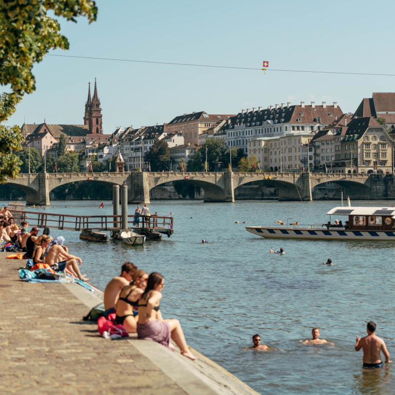 Badende Menschen im Rhein und am Rheinufer in Basel.