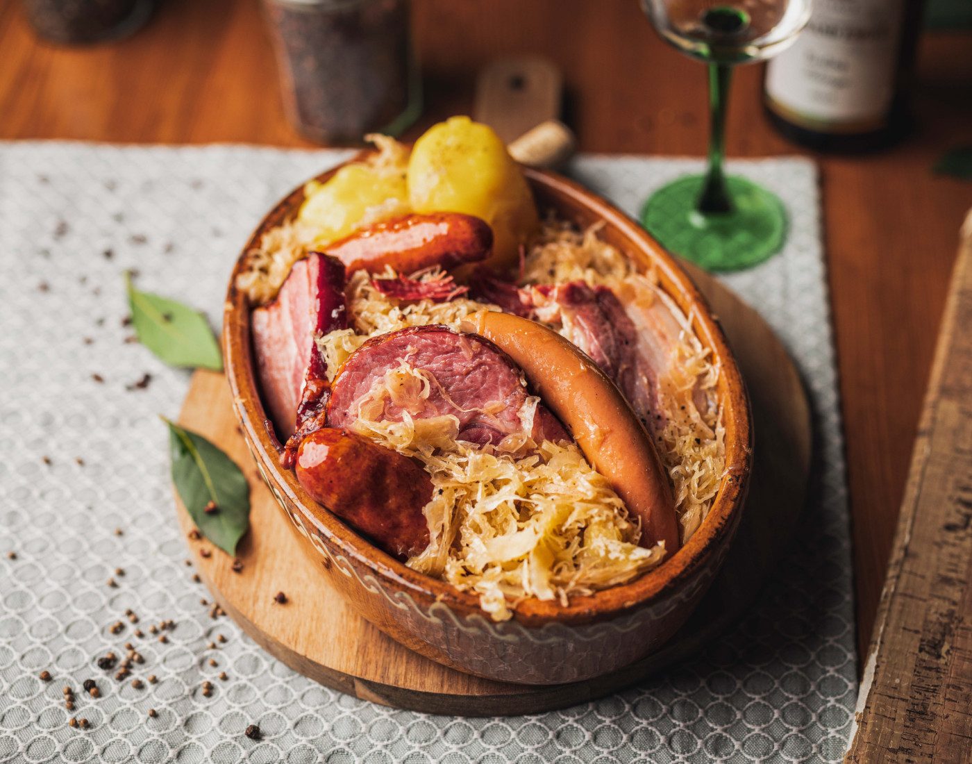 Ein Topf mit Sauerkraut, Fleisch, Würstchen und Knödel serviert auf Holzplatte auf einem Holztisch